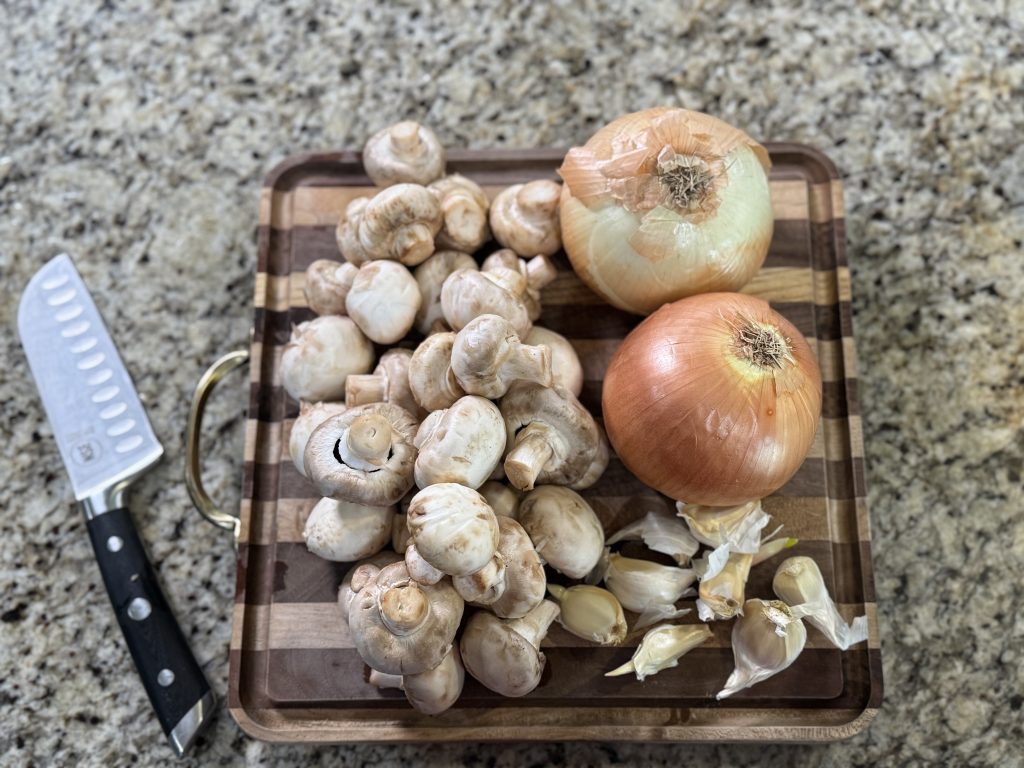 Homemade cream of mushroom soup ingredients on a cutting board with mushrooms, onions, garlic, and a knife