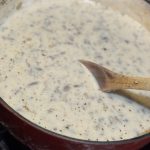 Thick homemade cream of mushroom soup simmering in a Dutch oven with a wooden spoon