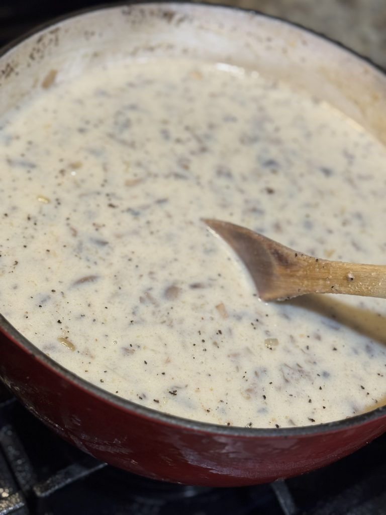 Thick homemade cream of mushroom soup simmering in a Dutch oven with a wooden spoon